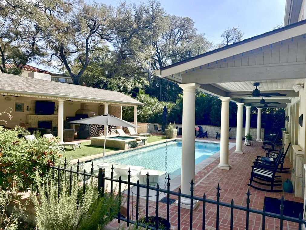 A back garden with a swimming pool, covered patio and brick terrace.